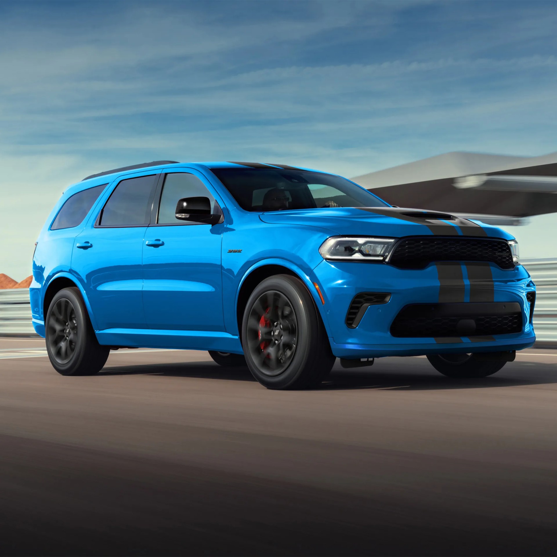 Blue Dodge Durango SUV with black racing stripes and black wheels driving on a road.