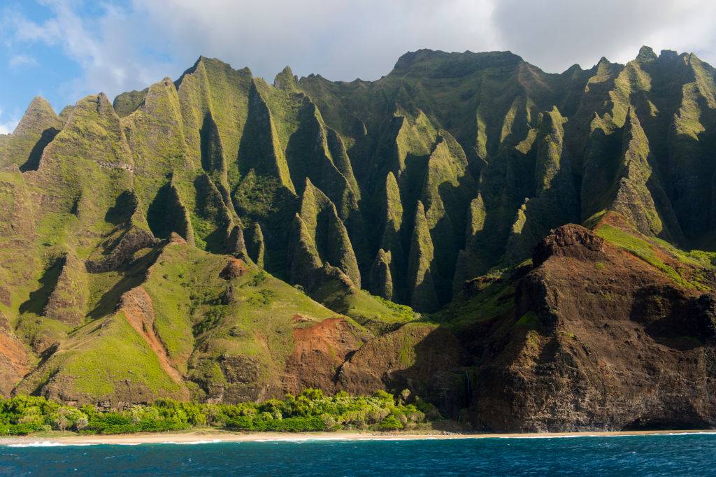 <p>It's a little tricky to see the Na Pali Coast in Kauai, Hawaii in person, but it can be done. The coastline is tucked away and can only be reached by helicopter, catamaran boat, or a vigorous hike through the lush green cliffs. Na Pali Coast was formed by volcanic eruptions over 70 million years ago.</p> <p>The tropical landscape on Kauai sets itself apart because of the vibrant flora and fauna surrounding the island. After the Na Pali Coast, the white-sand beaches of Poipu and the deep valleys of Waimea Canyon are perfect places to see what nature has to offer.</p>