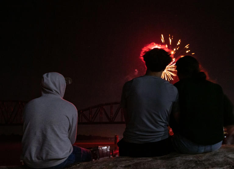 Landon Kirk (left) sits next to couple Kamden Davis and Raegan Blackburn as fireworks explode over the Ohio River during Tri-Fest in Henderson, Ky., Friday night, April 14, 2023.