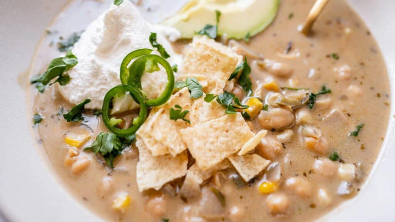 Close show of a bowl of tan chickpea chili garnished with sour cream and green herbs.