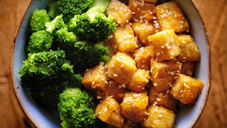 Close shot of a bowl with rice noodles, broccoli and tofu cubes.