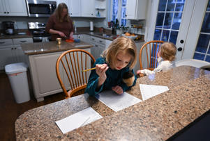 Aimee Beall works on homework beside Aurelia while their mother prepares a snack for them.