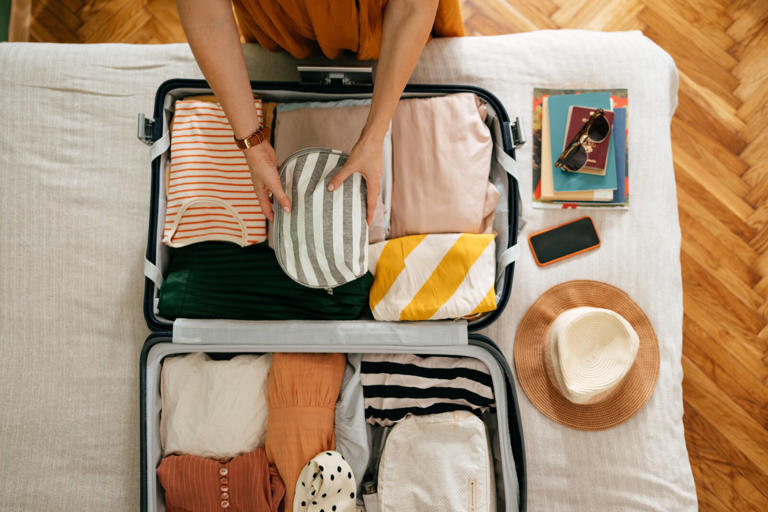 Shot from above of a woman packing items into her suitcase on a bed.