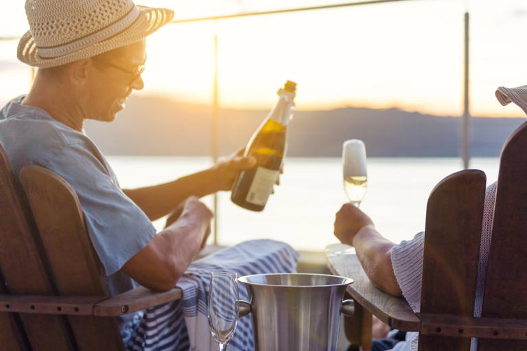 Man pouring his partner a glass of champagne at sunset on a cruise ship