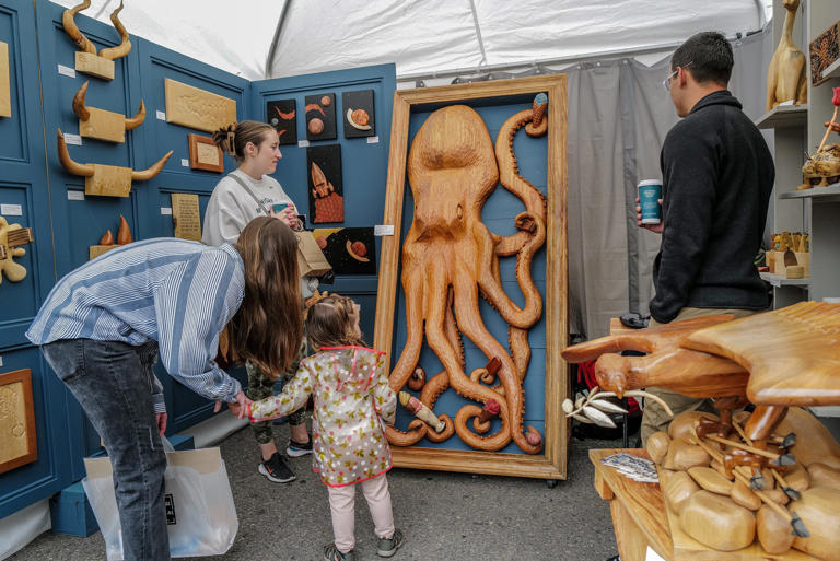 A child cautiously looks at a framed wood sculpture of an octopus by Faith Mebli at the East Lansing Art Festival Saturday, May 20, 2023.