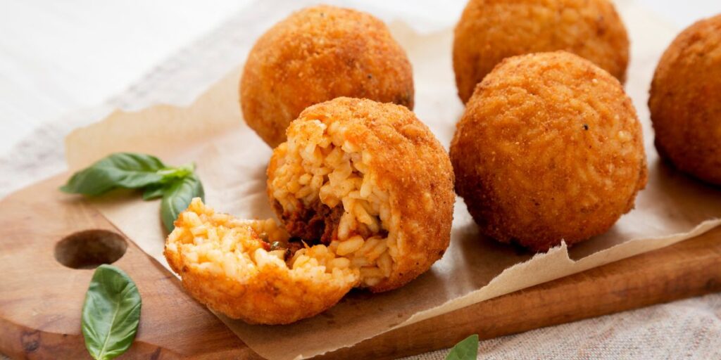 <p>Sicilian specialty of deep-fried rice balls stuffed with various fillings like ragù (meat sauce), mozzarella, and peas.</p>