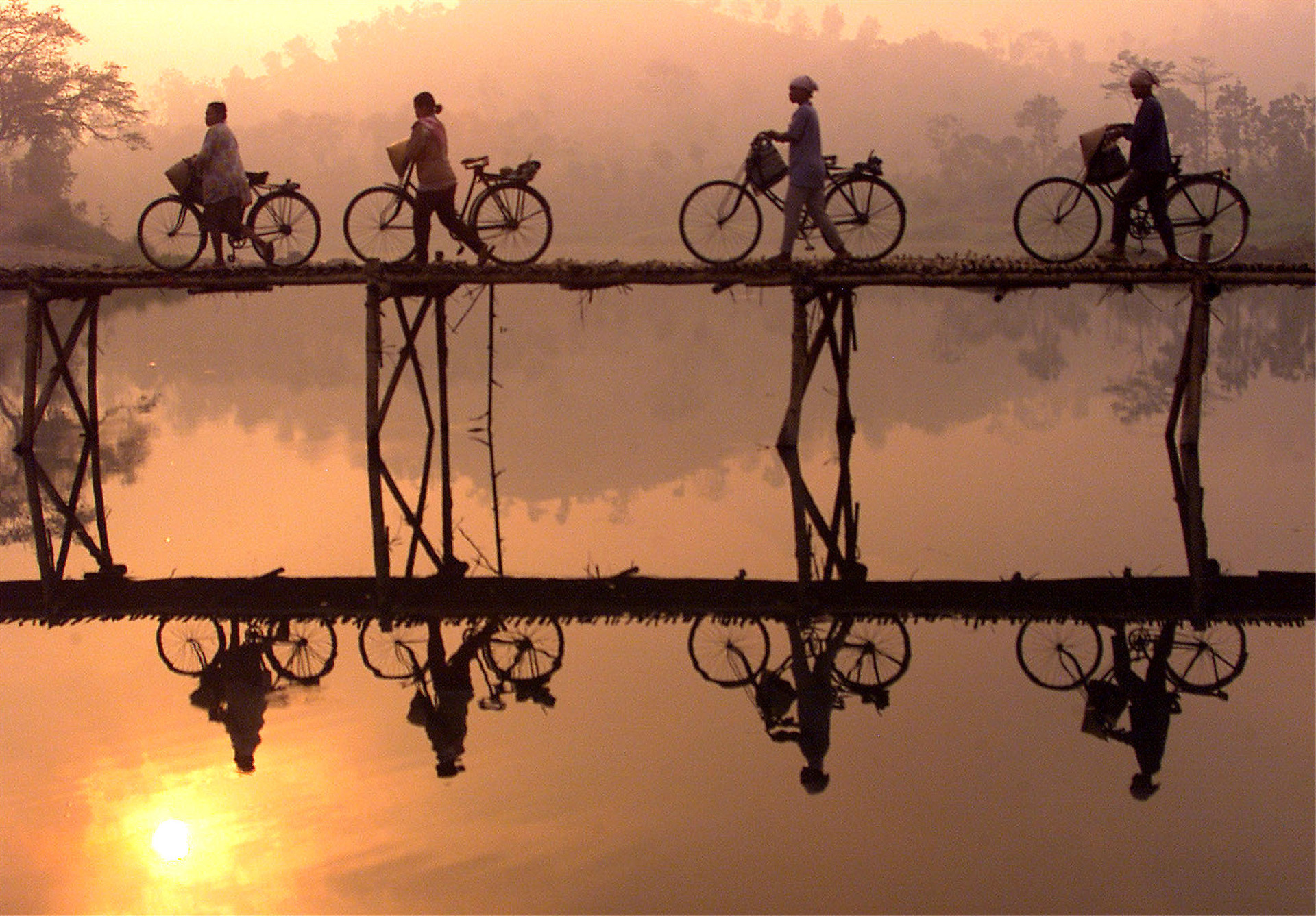 Des villageois traversent un pont de bambou avec leurs vélos alors que le soleil se lève derrière eux, non loin de la ville de Yogyakarta, dans le centre de Java.