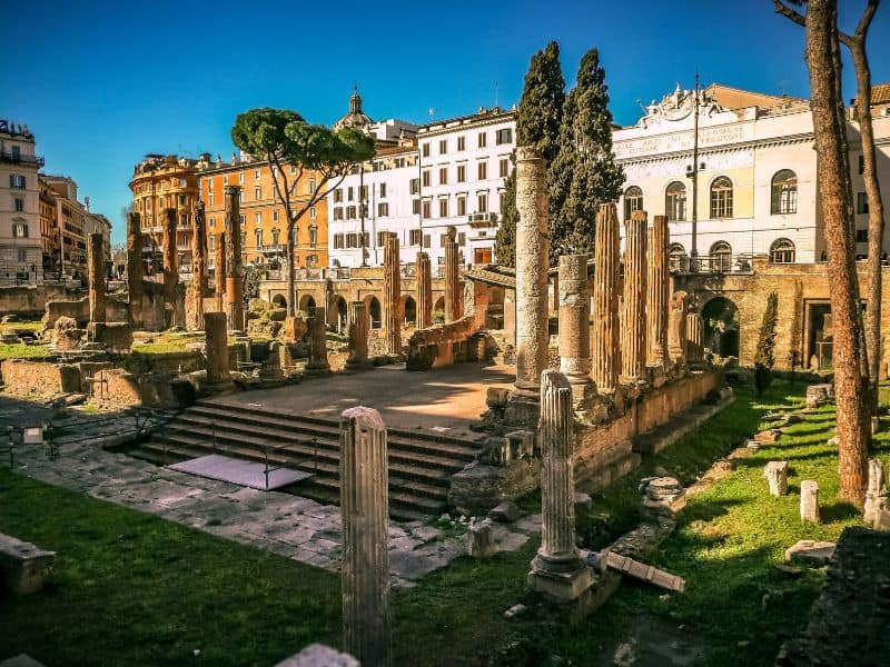 Captivating square dotted with the ruins of ancient Roman temples and surrounded by bustling buildings, where history seamlessly merges with the modern-day vibe of the city.