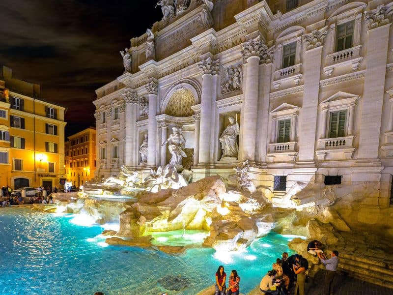 The iconic Trevi Fountain at night one of the best Rome Italy landmarks in 2023 with visitors gathered around its majestic marble structure and sparkling turquoise waters.