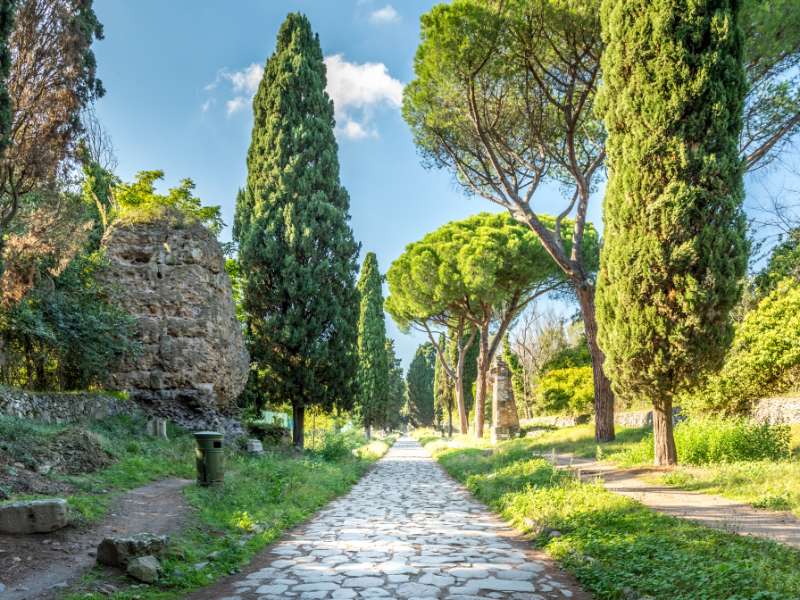 Via Appia Antica, Rome's ancient road full of history and charm. Imagine walking on old cobblestones, surrounded by lush green landscapes and remnants of ancient Roman tombs and monuments. 