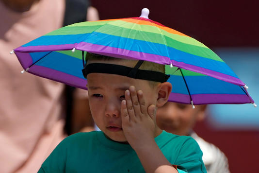 A boy wearing a rainbow umbrella wipes his sweat as he visits the Forbidden City on a sweltering day in Beijing, Friday, July 7, 2023. Earth's average temperature set a new unofficial record high on Thursday, the third such milestone in a week that already rated as the hottest on record.
