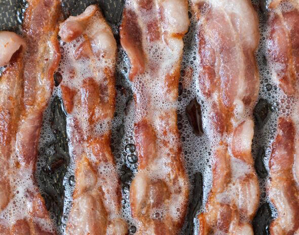 Above close-up view of bacon sizzling in frying pan