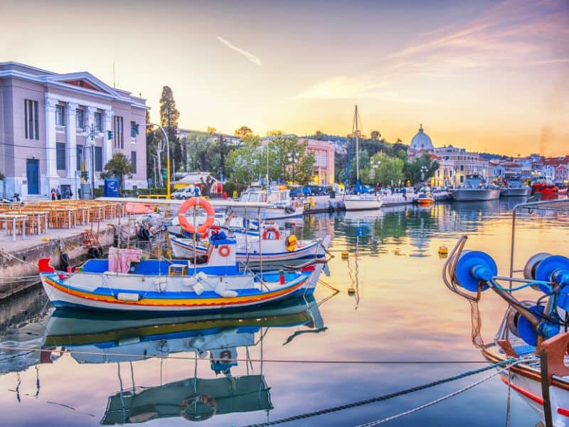 Boats on the water, reflecting the sunset with buildings in the background in Lesbos Greece