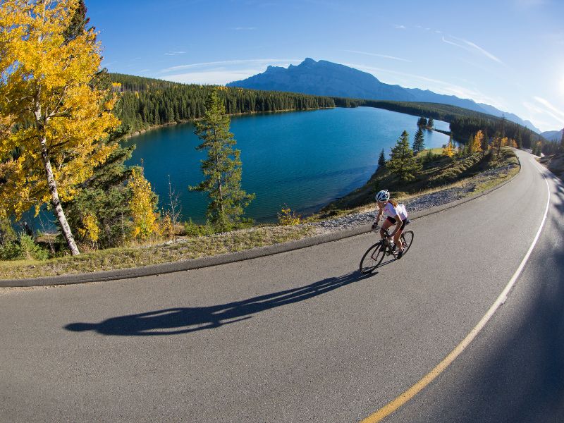 A woman confidently mountain biking through the scenic trails of Banff, enjoying the exhilaration of the ride while surrounded by stunning natural landscapes. majestic mountains and the wonderful lake.