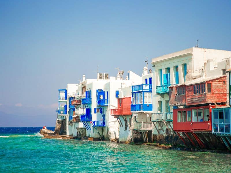 White buildings with blue and red balconies over the blue ocean in Little Venice, Mykonos