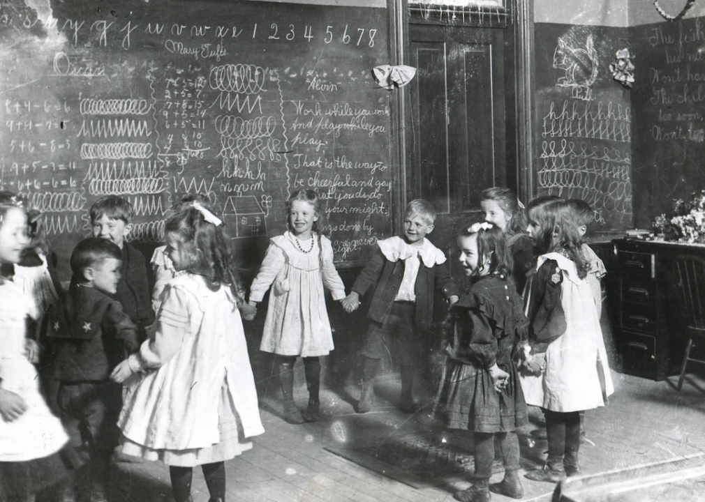 <p>The quality of <a href="https://pubs.lib.uiowa.edu/annals-of-iowa/article/4977/galley/113824/view/">schools in rural Iowa</a> in the 1890s was concerning to many who felt children were being disadvantaged by inferior education. This shortage of well-trained teachers was largely attributed to factors including subpar standards for teacher certification and low wages that left high-quality teachers disincentivized to educate children at Iowa schools. Children were often none the wiser, however, as is evident by this image of elementary school children holding hands and playing a game in their Keota, Iowa, classroom.</p>