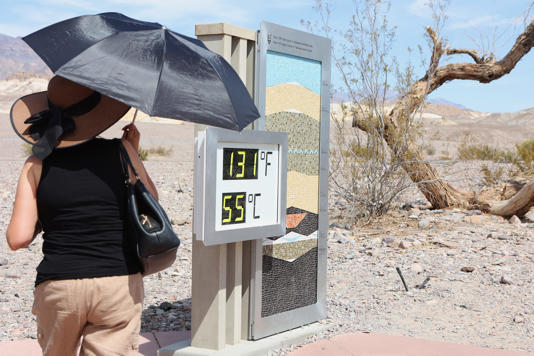 A woman stands near a digital display of an unofficial heat reading at Furnace Creek Visitor Center during a heat wave in Death Valley National Park in Death Valley, California, on July 16, 2023. California's famous Death Valley, one of the hottest places on Earth, reached 128 degrees Fahrenheit on Sunday.