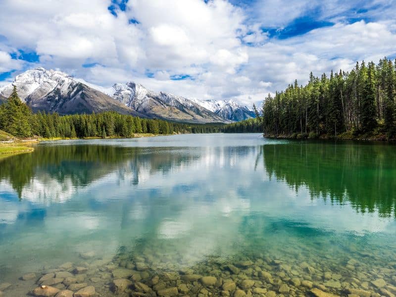 Clear emerald lake with snowcapped mountains and trees lining the shore