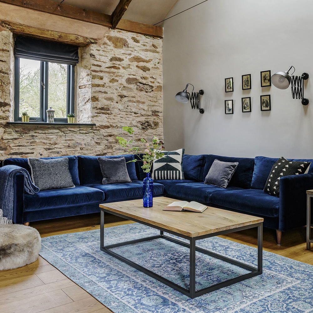 <p>                     A midnight blue velvet sofa has been contrasted with the distressed white stone wall in this living room in a converted barn. The sumptuous blue rather than looking cold against the white walls, creates a warm and inviting space to cosy up in. The rich blue colour scheme has been continued in the rug, and home accessories such as the vase and blanket.                   </p>