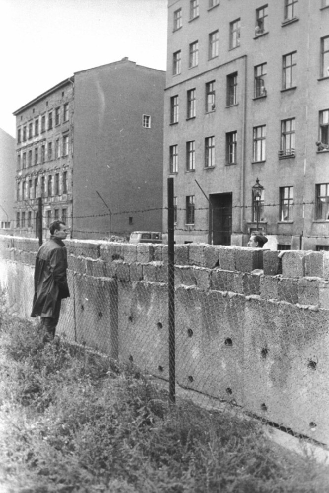 <p>Im Bild: Ein Mann in West-Berlin unterhält sich kurz nach dem Bau der Sperre über die Mauer hinweg mit seinem Ost-Berliner Nachbarn. Die Barrikade wurde bald erhöht und verstärkt, um solche Begegnungen zu verhindern.</p>