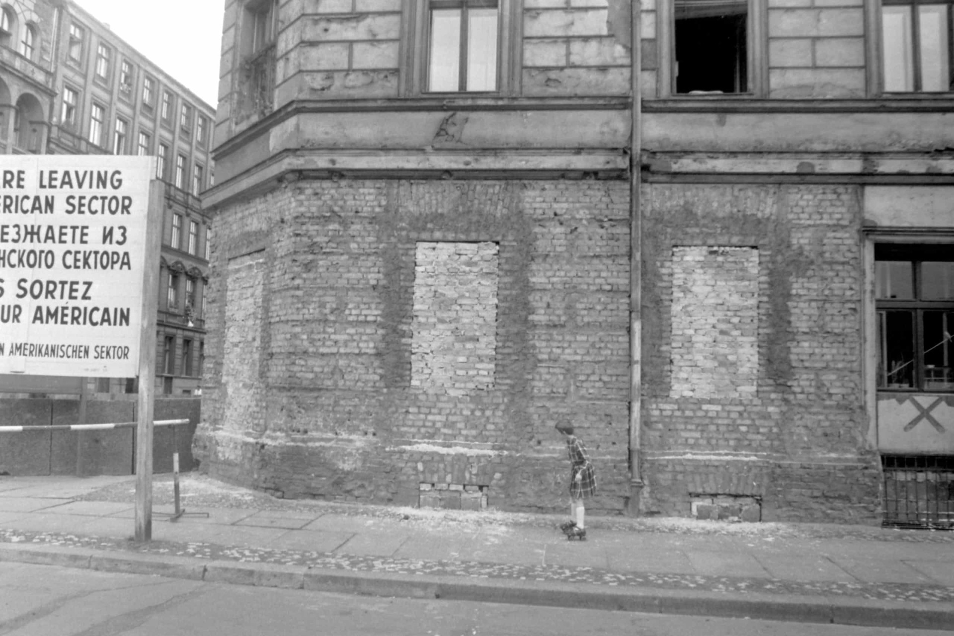 <p>Im Bild: Ein Kind auf Rollschuhen fährt die Luckauer Straße im Ostberliner Stadtteil Kreuzberg hinunter. Wegen der Nähe zur Mauer sind die Fenster im Keller des Hauses zugemauert, um einen Fluchtversuch in den Westen zu verhindern.</p>