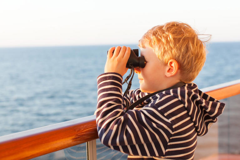 little boy using binoculars while on a cruise ship in open sea