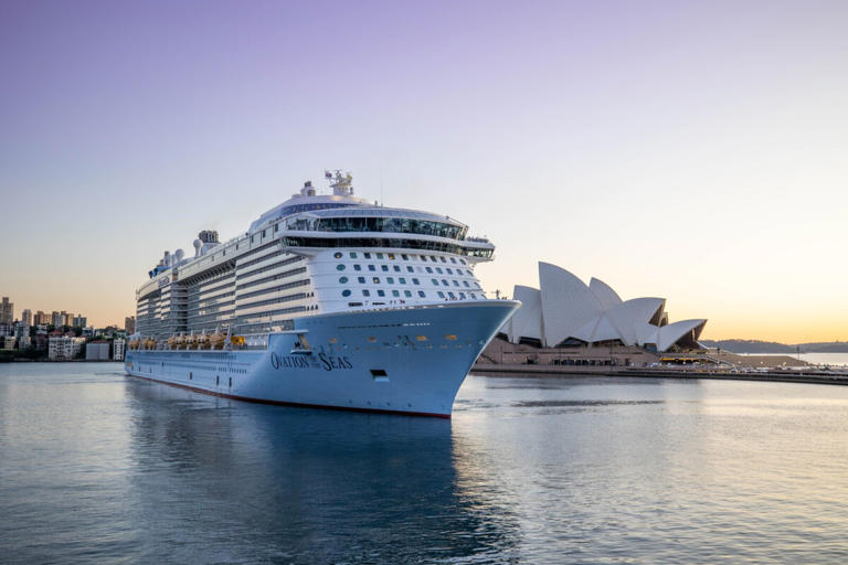 Royal Caribbean's Ovation of the Seas ship in front of the Sydney Opera House at sunset.