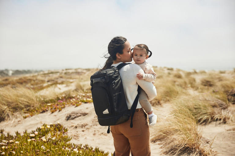 A mother holding her baby while wearing the No Reception Club The Getaway Bag in the desert.