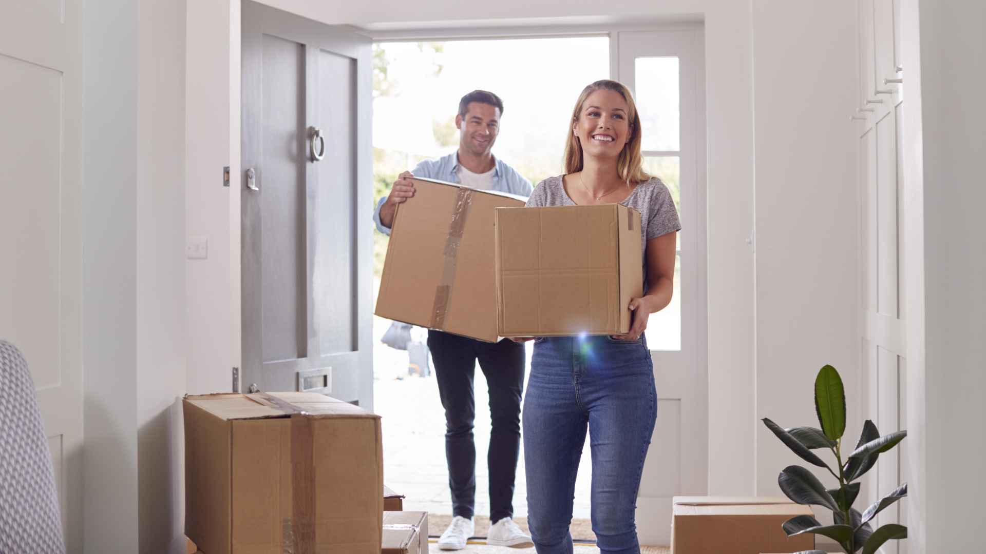 Excited Couple Carrying Boxes Through Front Door Of New Home On Moving Day