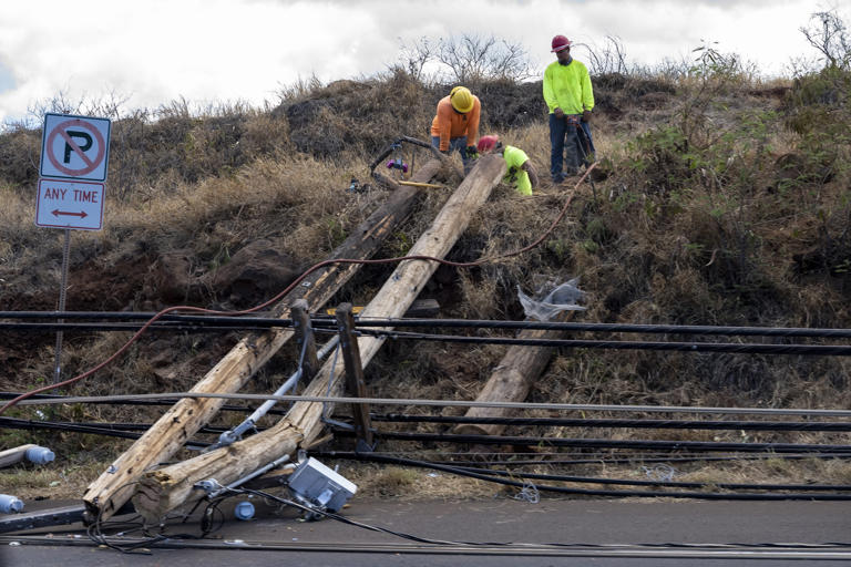 Workers of Maui Electric Company work on a fallen telephone pole on Honoapiilani Highway in Lahaina, Hawaii on August 11, 2023.