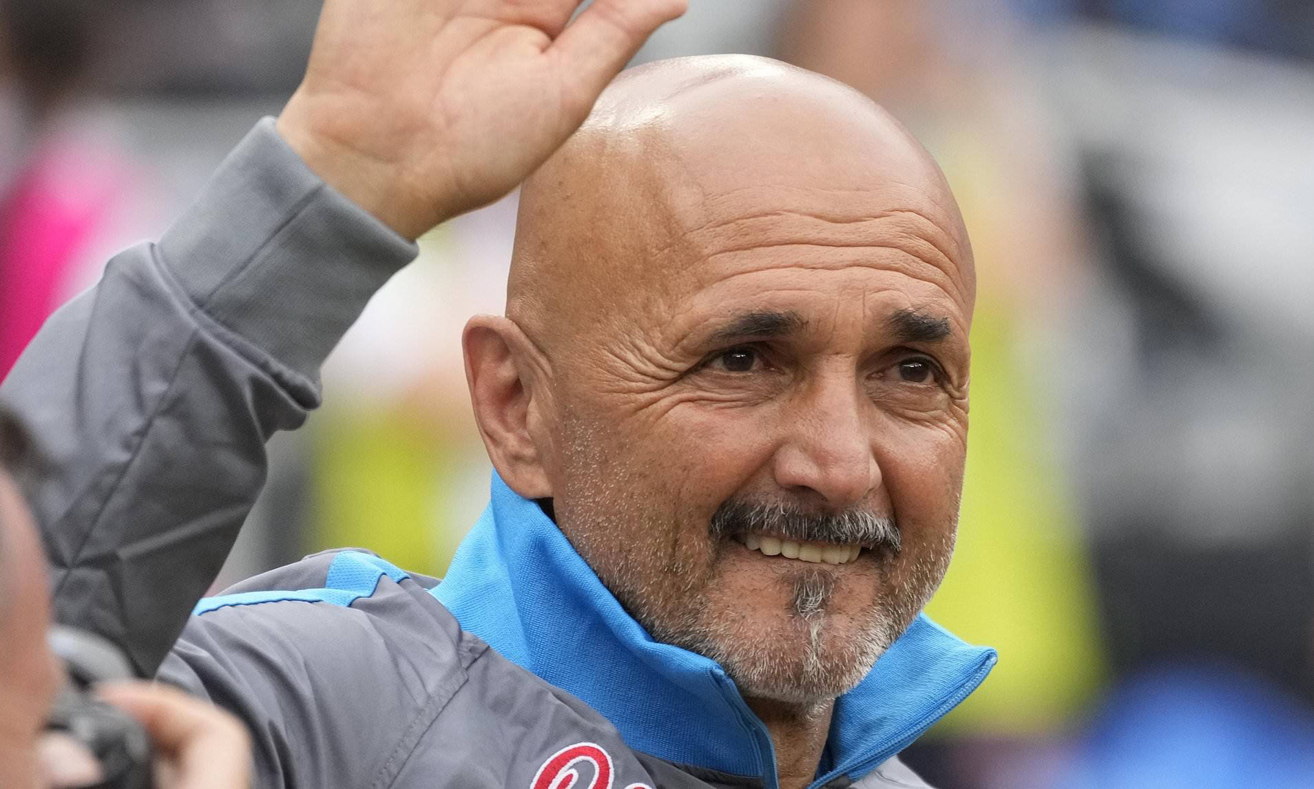  Luciano Spalletti, coach of SSC Napoli, wearing a grey cardigan sweater, blue collared shirt, and black pants while smiling and waving to the crowd.