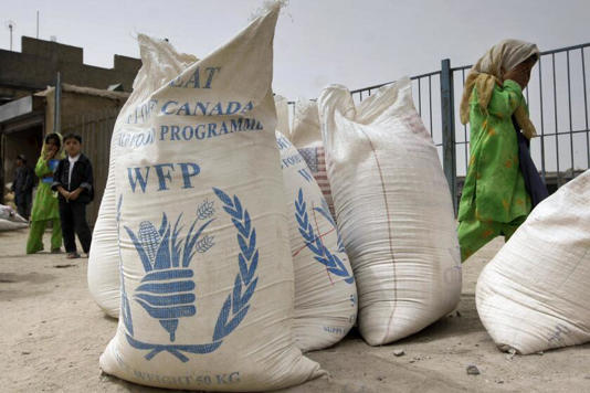 ARCHIVO - Una alumna de una escuela afgana, a la derecha, pasa junto a sacos de trigo molido con el logo del Programa Mundial de Alimentos en la calle principal de la ciudad de Kandahar, al sur de Kabul, Afganistán, el domingo 29 de junio de 2008. El Programa Mundial de Alimentos advirtió el martes que los recortes gubernamentales en el financiamiento humanitario han obligado a la agencia de Naciones Unidas a reducir de forma drástica las raciones de comida a los más hambrientos del mundo. ((Musadeq Sadeq / Associated Press))