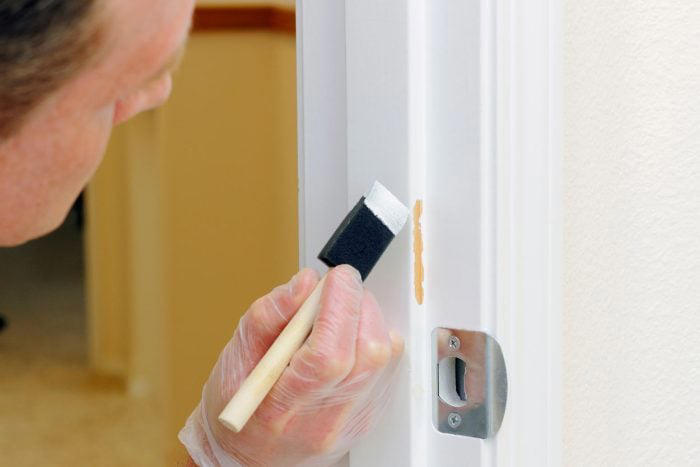 Mature white man in his forties about to paint a white door jam with touch up paint.