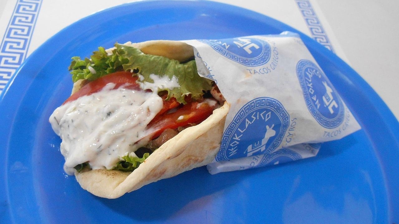 <p>A pita gyro is a traditional Greek <a href="https://wealthofgeeks.com/eat-like-local-while-traveling/">food</a>, and it can be found on every corner. It consists of shredded meat, usually pork, served with pita bread and fresh vegetables. Oh, and of course, don’t forget the tzaziki sauce, made from Greek yogurt, grated cucumbers, garlic, and dill.</p>