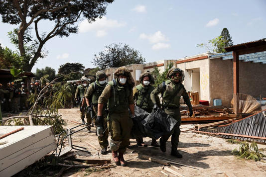 Soldados israelitas transportam o corpo de uma vítima dos ataques do Hamas em Kfar Aza