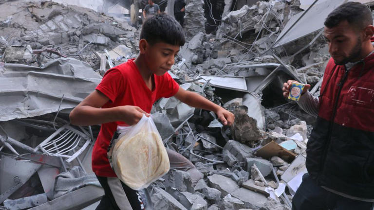 A Palestinian youth carries bread amid the rubble of the city center of Khan Yunis in the southern Gaza Strip following Israeli shelling on October 10. - Said Khatib/AFP/Getty Images