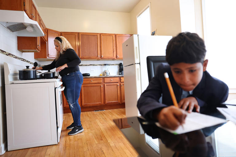 Venezuelan migrant Yohana Maria Moreno Muñoz, 39, prepares dinner as her younger son, Isaac, 11, does homework at their apartment on Oct. 18, 2023.