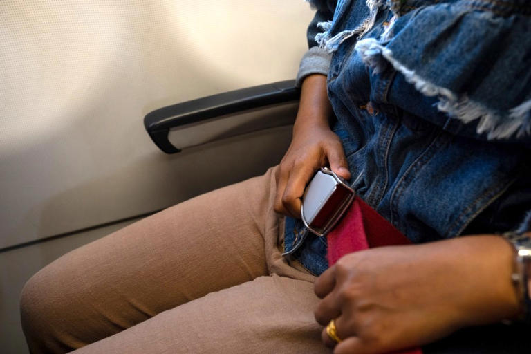 A female traveler buckles herself into an airline seat