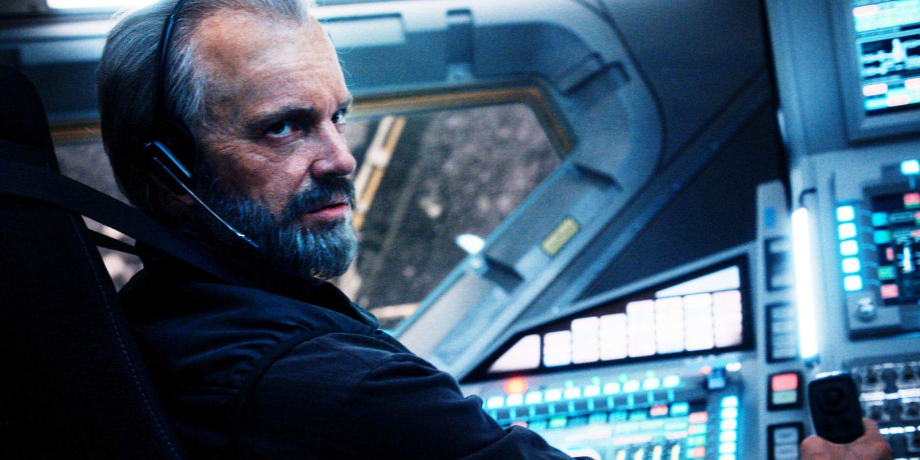 An astronaut with grey hair and beard pilots a spaceship. 