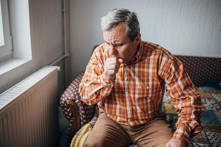 One man, worried senior man, sitting alone at his home. He has a pain in his knee.