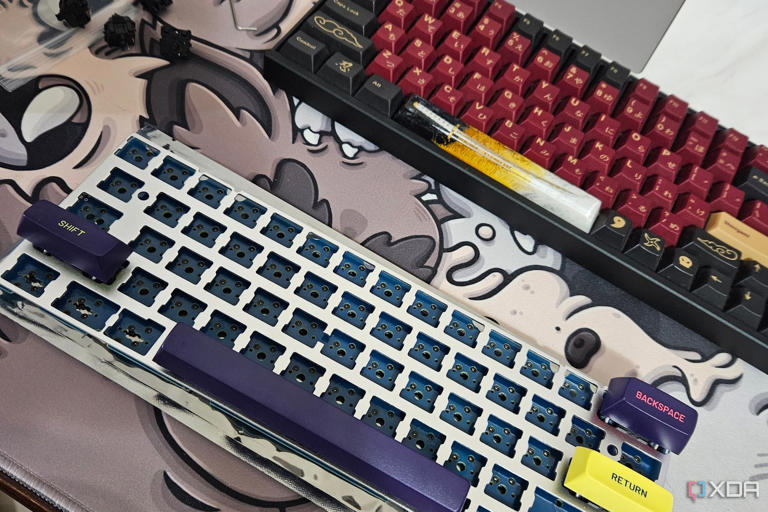 A disassembled mechanical keyboard with a yellow case and purple keycaps next to an assembled Keychron K2V2 mechanical keyboard.