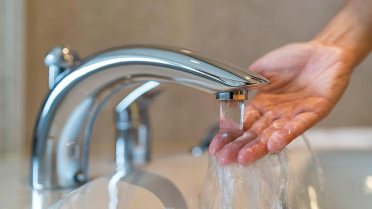 Person with hand under running faucet 