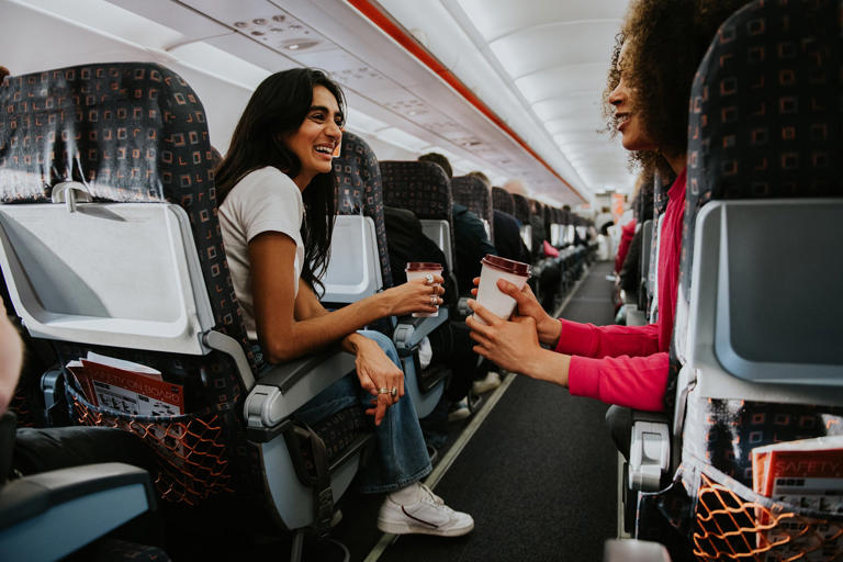 Two woman drink coffee and have a light hearted chat on a plane