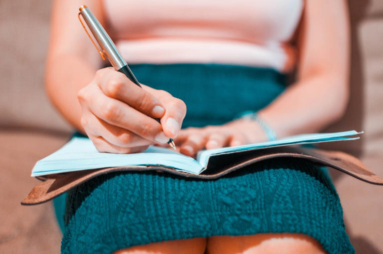 A young woman is writing on her journal while sitting on a couch