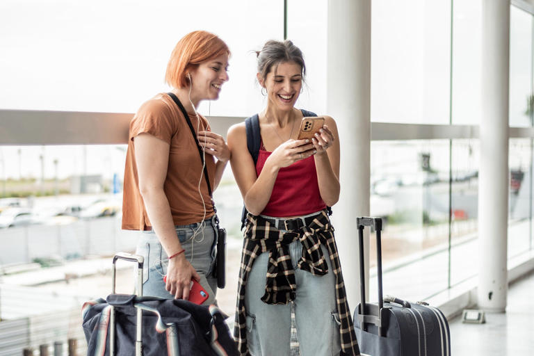 Young friends woman using mobile phone while waiting at airport