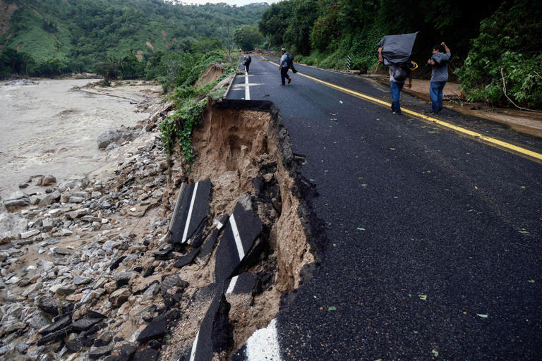 People pass by part of a road which was washed away at the Kilometro 42 community, near Acapulco, Guerrero State, Mexico, after the passage of Hurricane Otis, on October 25, 2023. Nearly four in 10 people believe that they will be displaced in the next 25 years because of the effects of climate change according to a new study by Ipsos.