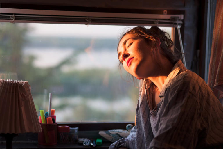 young woman enjoying morning sun next to her window
