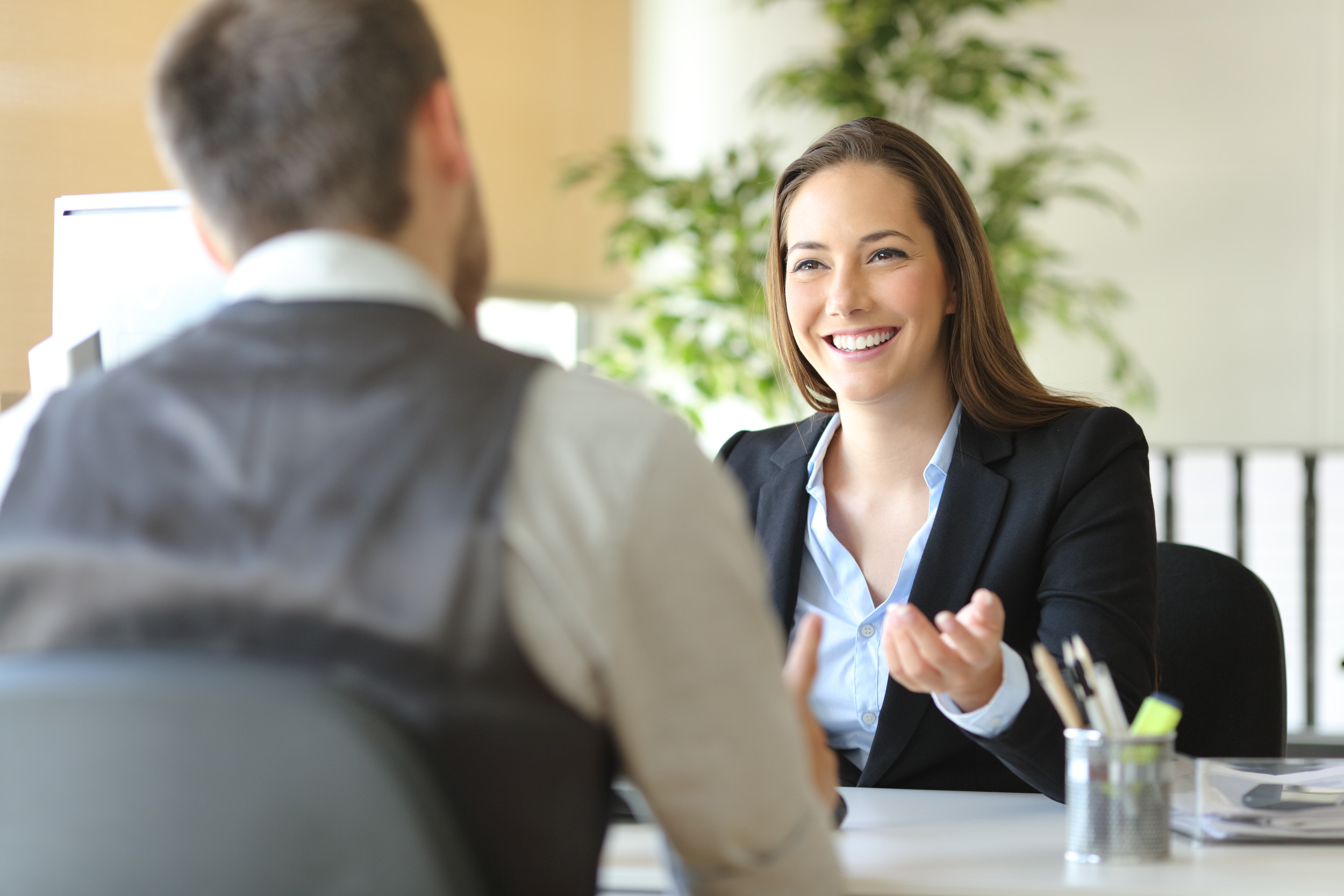 A stock image of a woman smiling while speaking to a man at a desk. "The most common reason it can be difficult to ask directly for a promotion is that it’s simply awkward to discuss money with your boss” and it can feel uncomfortable," a psychologist and business coach told Newsweek.