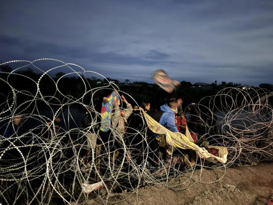 After wading across the Rio Grande near Eagle Pass, migrants attempt to get past the razor wire set up by Texas state officials. / Credit: Camilo Montoya-Galvez