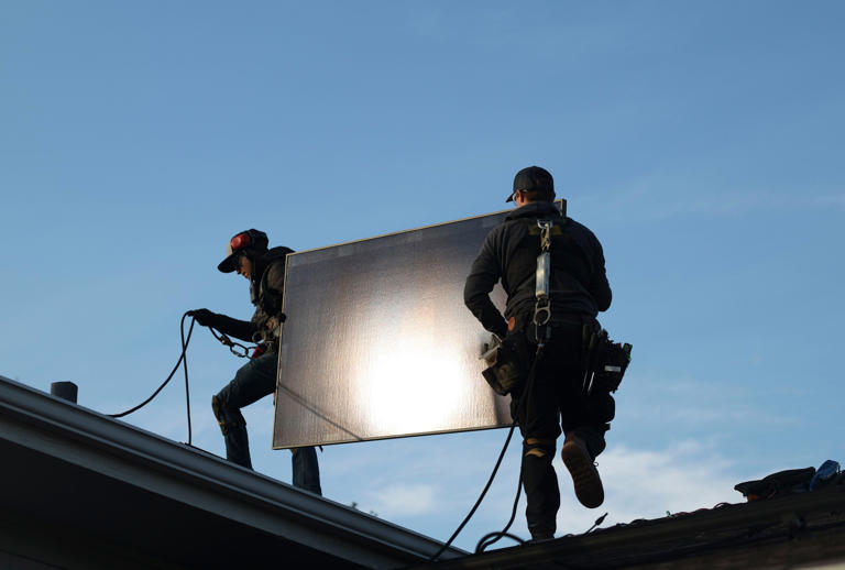 Garrison Riegel, left, and Jared Salvatore carry a solar panel onto a roof in Schaumburg, Nov. 30, 2023.